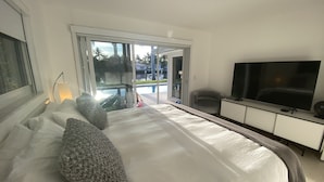 Une chambre d’hôtel avec un grand lit, une télévision, un bureau et une vue sur la piscine, visible à travers les portes vitrées.