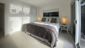 Une chambre à coucher comprenant un lit, des tables de chevet, une fenêtre et une porte-fenêtre coulissante.