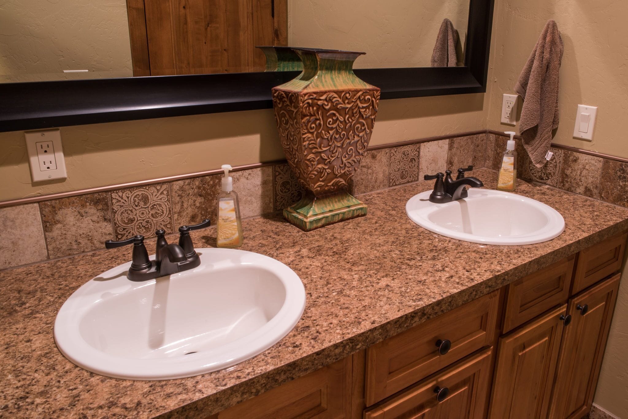 A bathroom with two sinks, a mirror, a decorative vase, and a towel rack.
