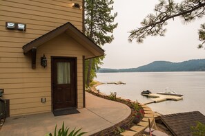 A house with a wooden exterior, a front door, and a porch leading to a lake with boats.