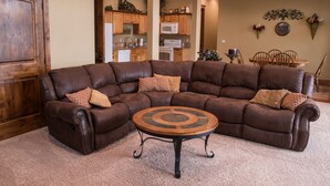 A sectional sofa with a round coffee table in a living room with a kitchen in the background.