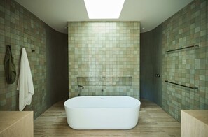 A modern bathroom with a freestanding bathtub, tiled walls, and a skylight.