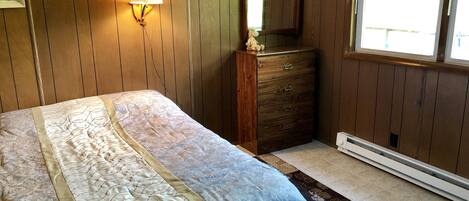 A bedroom with a bed, a dresser, a wall-mounted lamp, a mirror, and a window.
