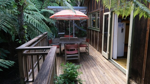 Une terrasse en bois avec une table et des chaises, entourée de fougères luxuriantes et d’une clôture en bois.