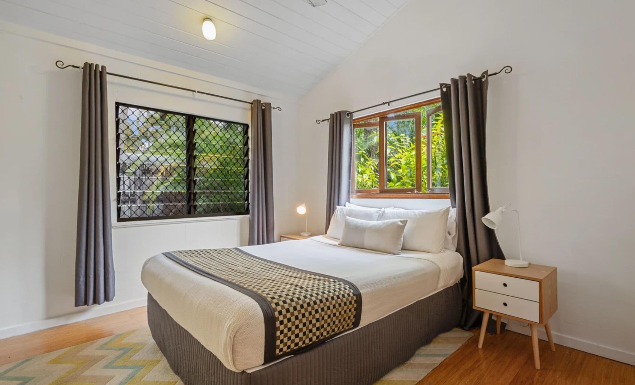 A bedroom with a bed, a nightstand, a window with curtains, and a view of greenery outside.