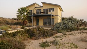 Un bâtiment à deux étages doté d’un balcon, entouré d’une végétation luxuriante et d’un terrain sablonneux.