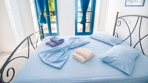 A bed with blue and white linens, a metal frame, and a view of the outdoors through a window with blue curtains. - Sea view house with swimming pool ISLA summer homes (Paros)
