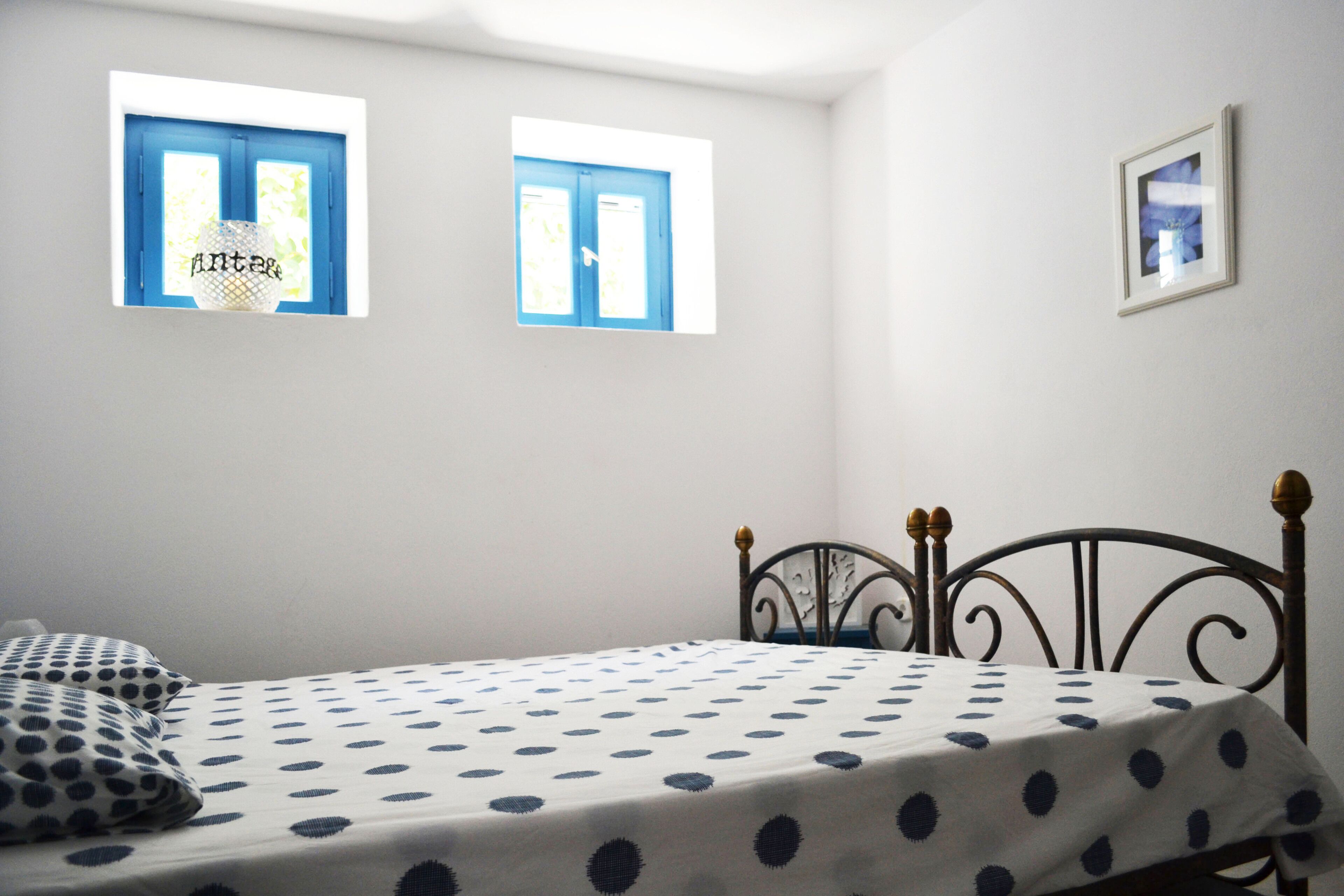 A bedroom with a bed, two windows, and a framed picture on the wall.