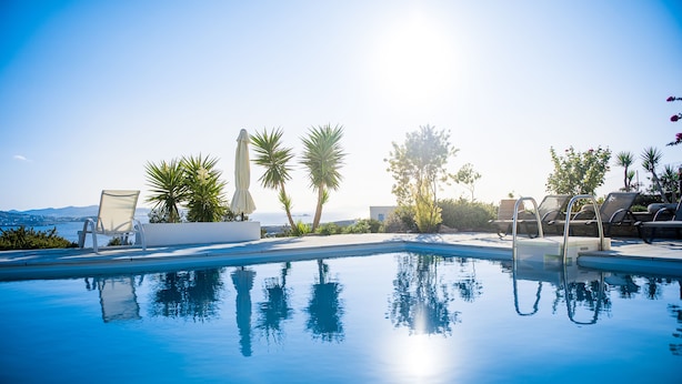 A clear blue pool with lounge chairs and umbrellas, surrounded by palm trees and a view of the ocean. - Sea view house with swimming pool ISLA summer homes (Paros)