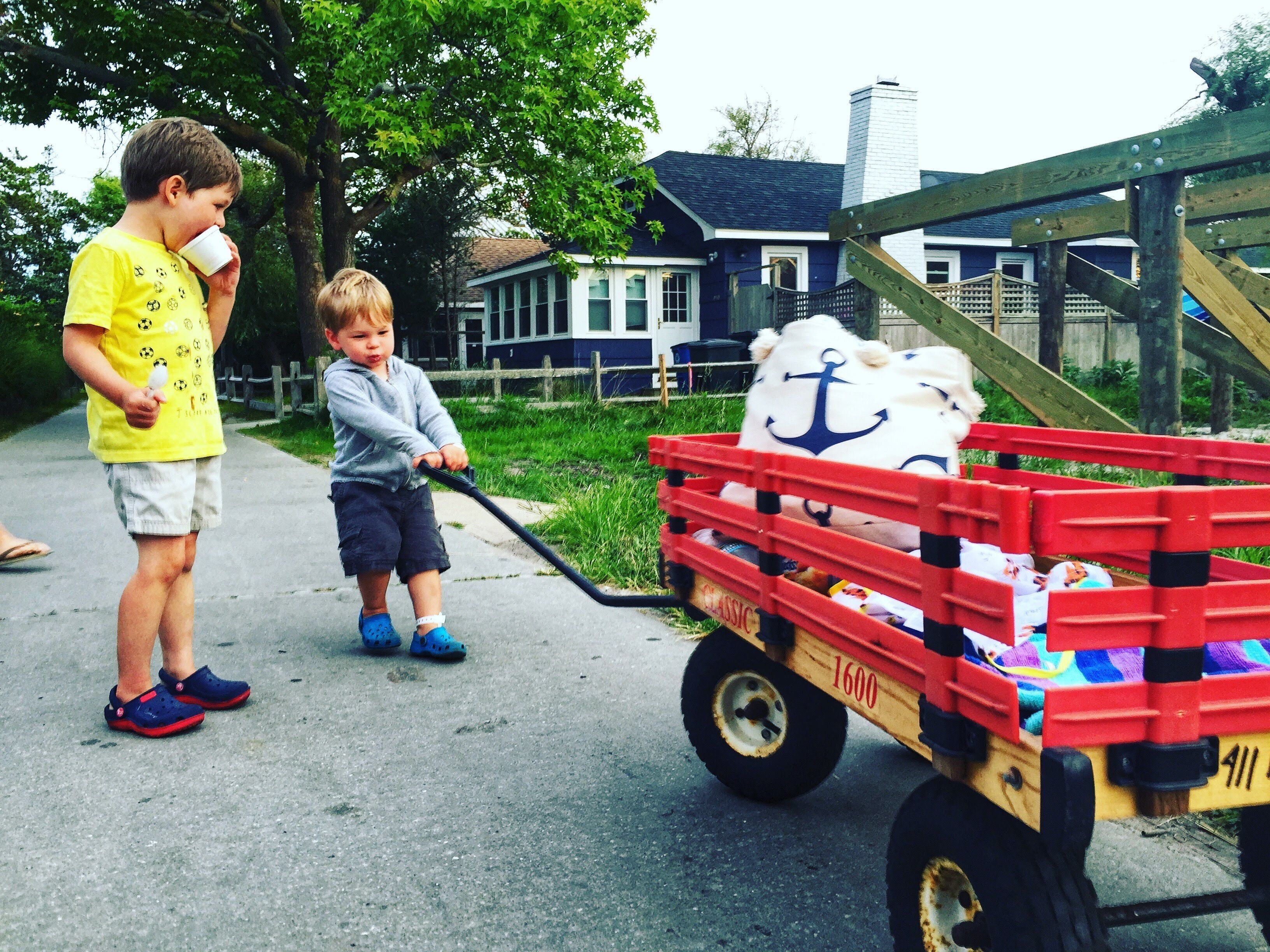 Deux enfants jouent avec un petit chariot jouet sur un trottoir.
