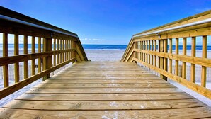 A wooden boardwalk leading to a beach with a clear blue sky.