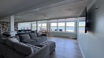 Un salón amplio con un sofá seccional gris grande, una pared de acento de piedra y vistas al agua a través de ventanas grandes.