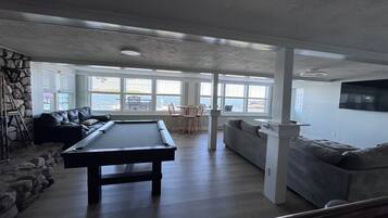 A spacious living area with a pool table, seating, and large windows overlooking a body of water.