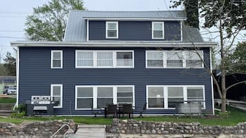 A two-story house with a dock extending into a body of water, stone walls, and outdoor furniture.