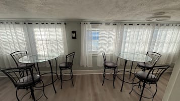 A dining area with round glass tables and black metal chairs, surrounded by white curtains and a view of the sea.