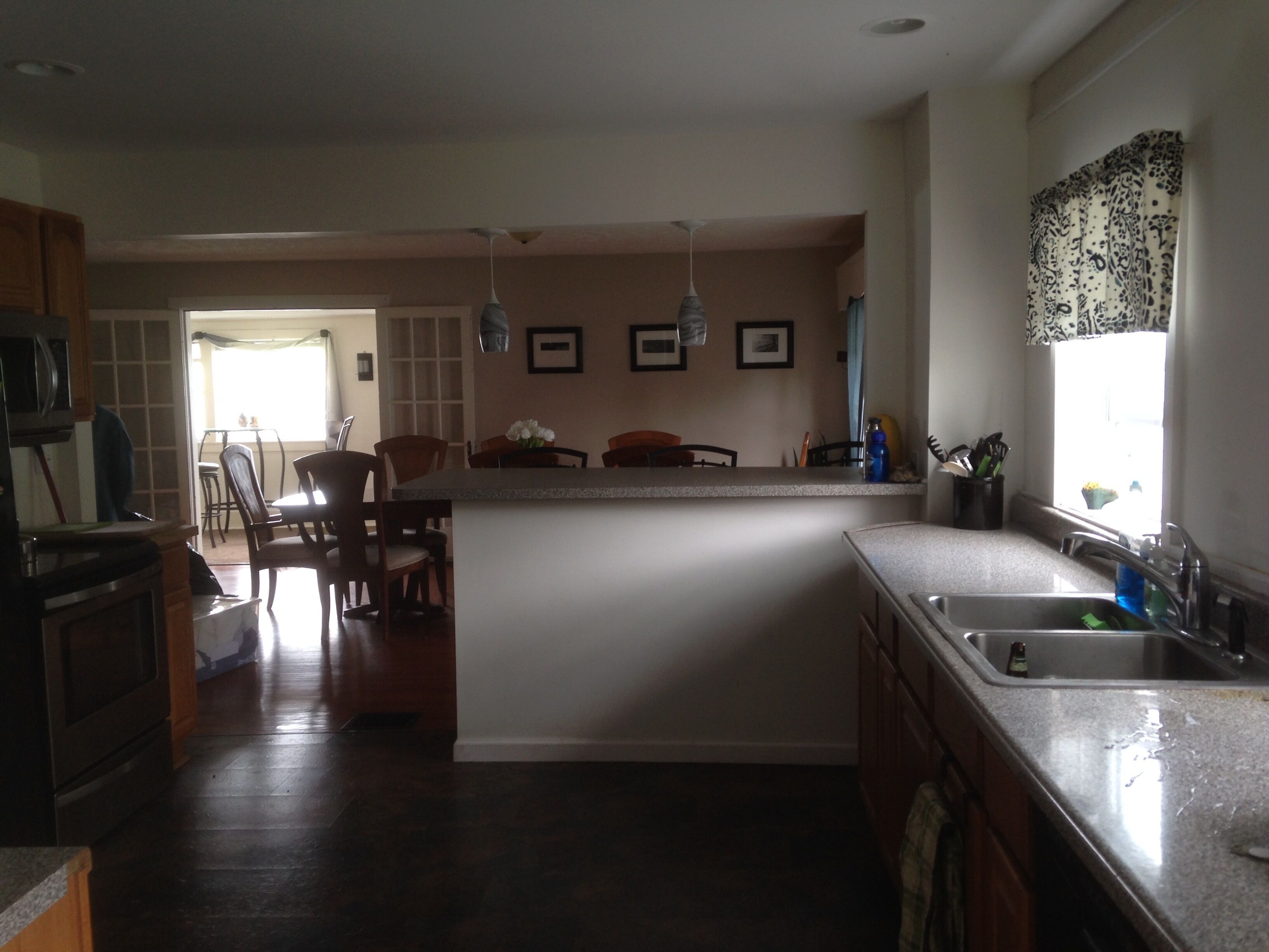 A kitchen with a central island, wooden cabinets, a dining area with chairs, and a window with patterned curtains.