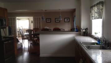 A kitchen with a central island, wooden cabinets, a dining area with chairs, and a window with patterned curtains.