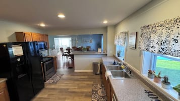 A modern kitchen with granite countertops, a black refrigerator, and a dining area with wooden chairs.