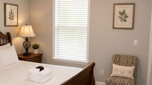 Een slaapkamer met een houten bed, een nachtkastje met een lamp, een stoel en een raam met jaloezieën.