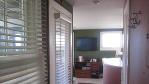 A hallway with a door leading to a bathroom, a television mounted on the wall, and a striped rug on the floor. - Blue Harbor Haven - West End Waterfront Condo with Stunning Harbor Views! (Provincetown)