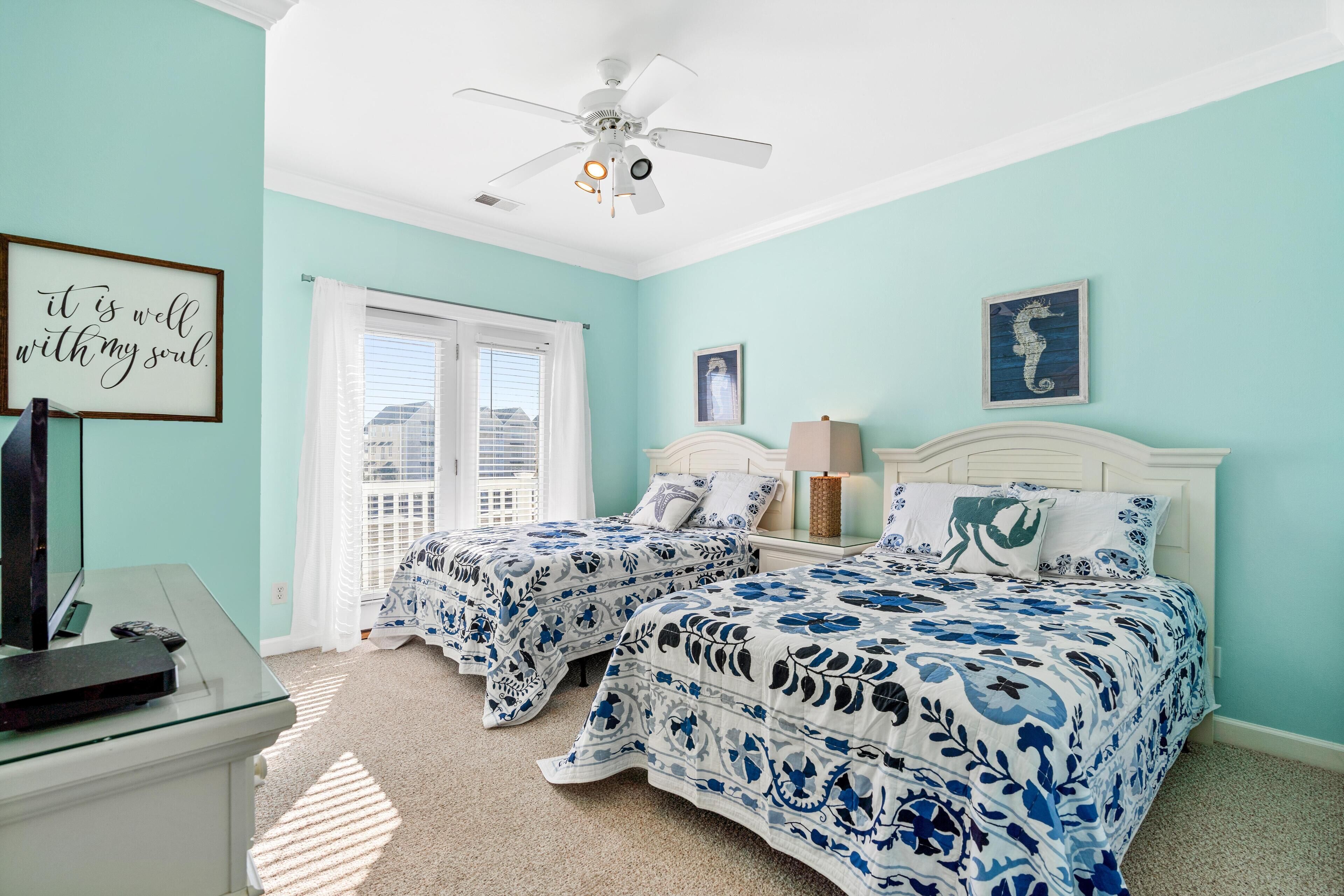 A bedroom with two beds, a ceiling fan, a desk with a computer, and a window with blinds.