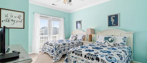 A bedroom with two beds, a ceiling fan, a desk with a computer, and a window with blinds.