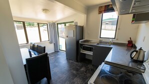 A compact kitchen with a refrigerator, stove, sink, and a dining area with a chair. - Amazing LakeVista House (Mangakino)