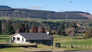 A rural house with a satellite dish, surrounded by a grassy field and a forested hill. - Amazing LakeVista House (Mangakino)