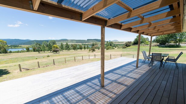 A wooden deck with a pergola, outdoor furniture, and a view of a lake and hills. - Amazing LakeVista House (Mangakino)