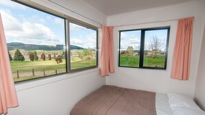 A bedroom with two windows, a bed, and a view of a green landscape. - Amazing LakeVista House (Mangakino)