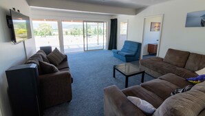 A living room with a sofa set, a coffee table, and a flat-screen TV mounted on the wall. - Amazing LakeVista House (Mangakino)