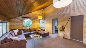 A modern living room with a brick wall, a round window, a sofa, a coffee table, and a door. - Fern Ridge Private Resort/ Wedding / Function Venue (Coffs Harbour)
