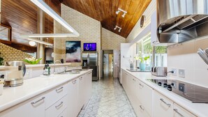 A modern kitchen with white cabinetry, stainless steel appliances, and a wooden ceiling. - Fern Ridge Private Resort/ Wedding / Function Venue (Coffs Harbour)