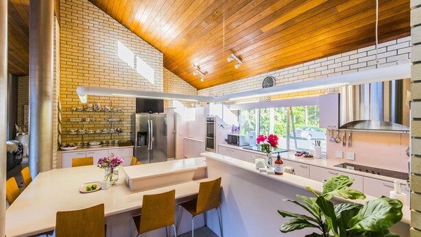 A modern kitchen with a brick wall, stainless steel appliances, and a dining area with a white table and chairs. - Fern Ridge Private Resort/ Wedding / Function Venue (Coffs Harbour)