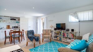 A living room with a sofa, chairs, a TV, a bookshelf, and a kitchen area with cabinets and a microwave.