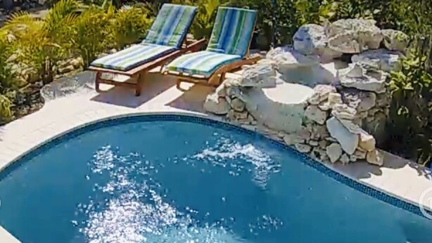 Una piscina con dos sillas reclinables y un muro de piedra.