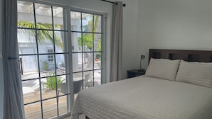 Un dormitorio con una cama grande, una mesita de noche, una ventana con cortinas y vistas al jardín exterior.