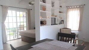 Un comedor con una mesa lista para dos personas, un sofá y una estantería con objetos decorativos.
