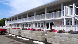 A two-story building with a balcony, stone retaining walls, and flower beds.