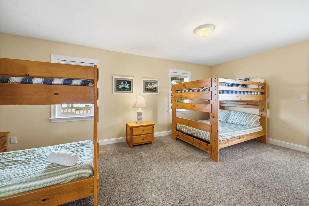 A room with two bunk beds, a small bedside table with a lamp, and framed pictures on the wall.