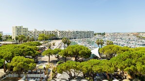 A marina with numerous boats, a large hotel building in the background, and lush green trees in the foreground. - 🌴 Sunny 3-Bedroom Marina Apartment | Sea Views | Secure Parking | Beach Walk (Mauguio)
