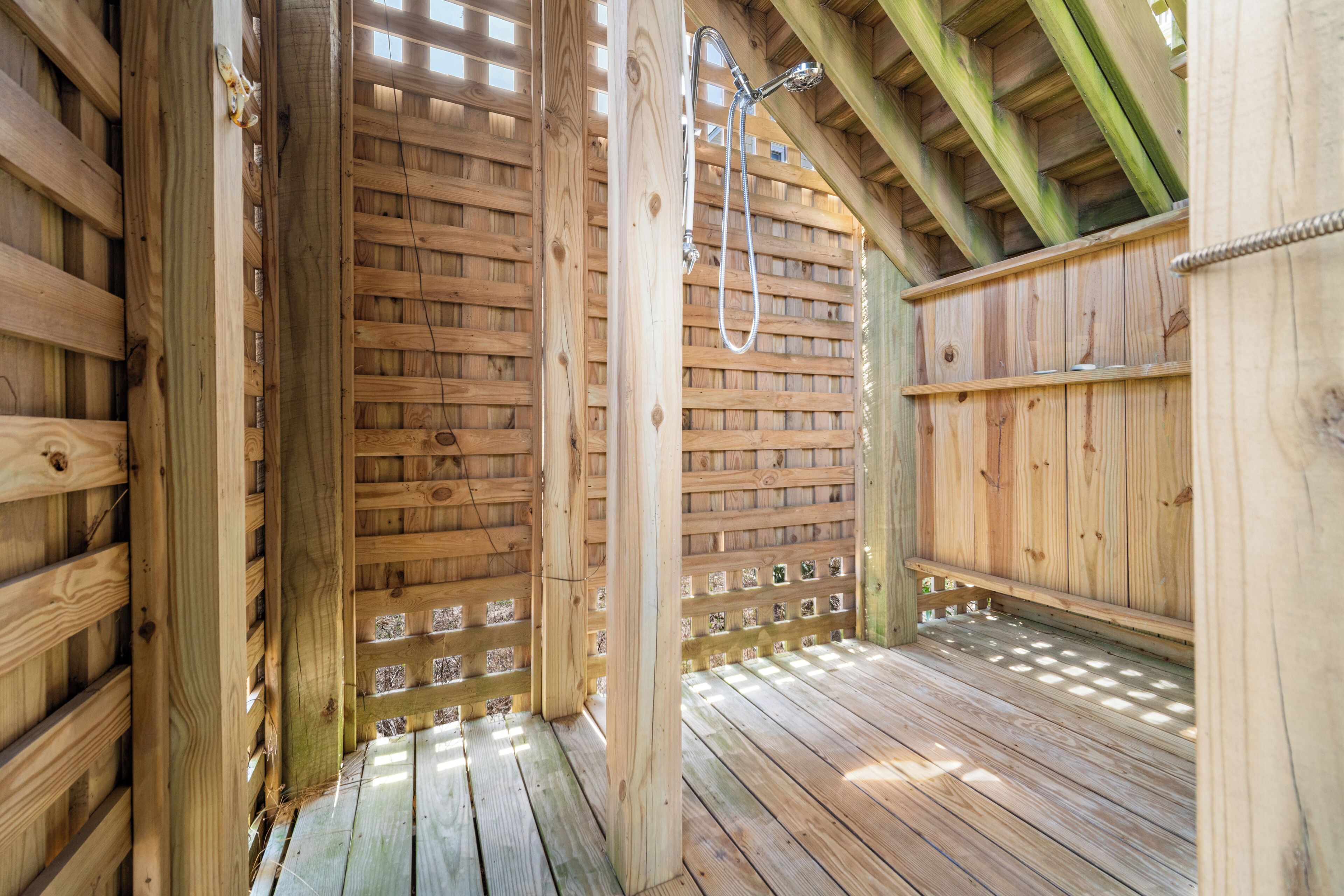 A wooden deck with a shower area, wooden walls, and a sloped ceiling.