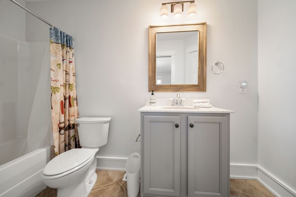 A bathroom with a toilet, a sink, a mirror, and a shower curtain.