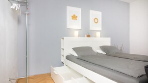 Un dormitorio moderno con una cama, un armario blanco y un box de ducha de vidrio.