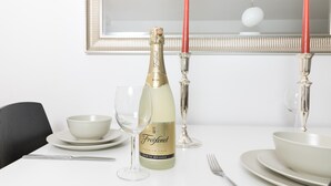 Una mesa de comedor dispuesta con una botella de Freixenet, dos velas rojas y vajilla blanca.