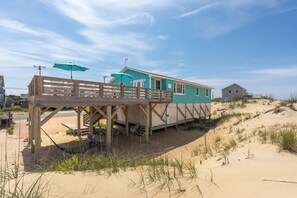 Una casa sulla spiaggia con una terrazza in legno, un portico coperto e una spiaggia sabbiosa.