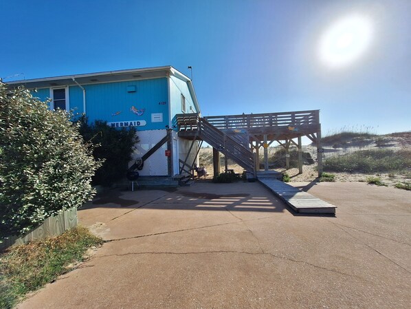 A blue building with a wooden deck and a staircase leading to a beach area. - Oceanfront home featuring 500 square foot Oceanfront deck! (Kitty Hawk)