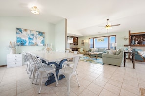 A spacious living room with a dining area, a kitchen, and a view of the ocean.
