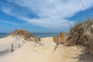 A sandy beach path leading to the ocean, with wooden barriers and sparse vegetation.