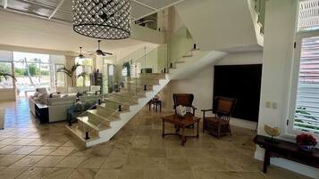 A spacious interior with a staircase, seating area, and a large chandelier.